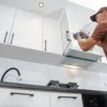 A professional installer working on white kitchen cabinets, illustrating how cabinet refacing works step by step in an Oakland County home.