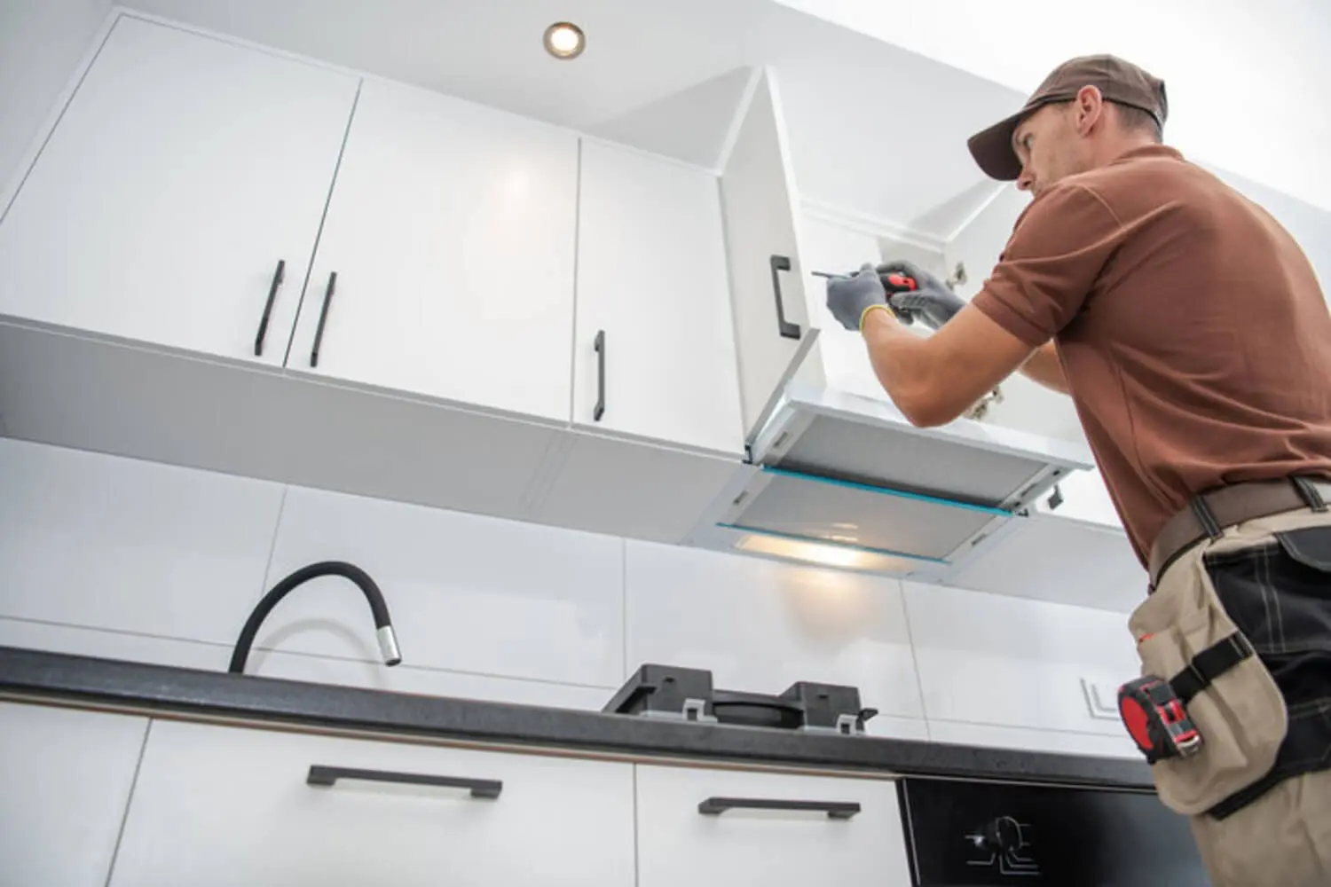 A professional installer working on white kitchen cabinets, illustrating how cabinet refacing works step by step in an Oakland County home.