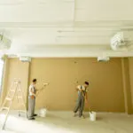 Two professional painters rolling paint on the interior walls of a commercial facility, illustrating how facility maintenance painting works in an active building.