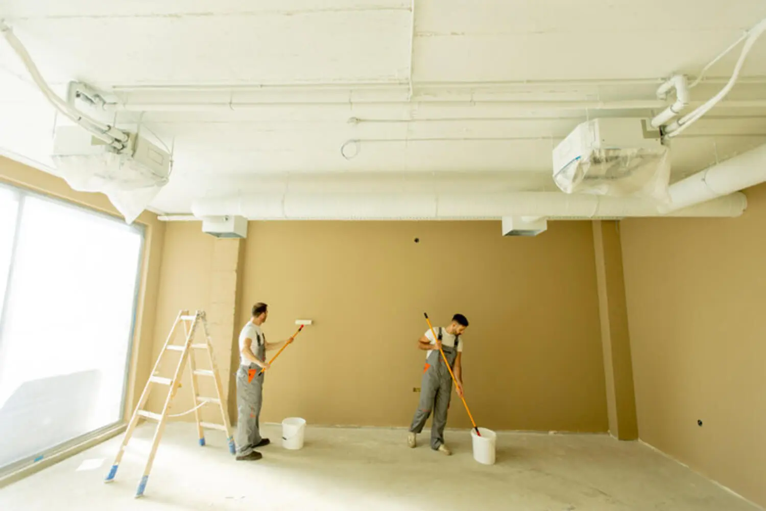 Two professional painters rolling paint on the interior walls of a commercial facility, illustrating how facility maintenance painting works in an active building.