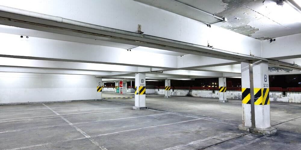 Commercial parking garage interior with deteriorating paint on the ceiling, exposed concrete surfaces, and safety-striped support columns showing signs of wear.