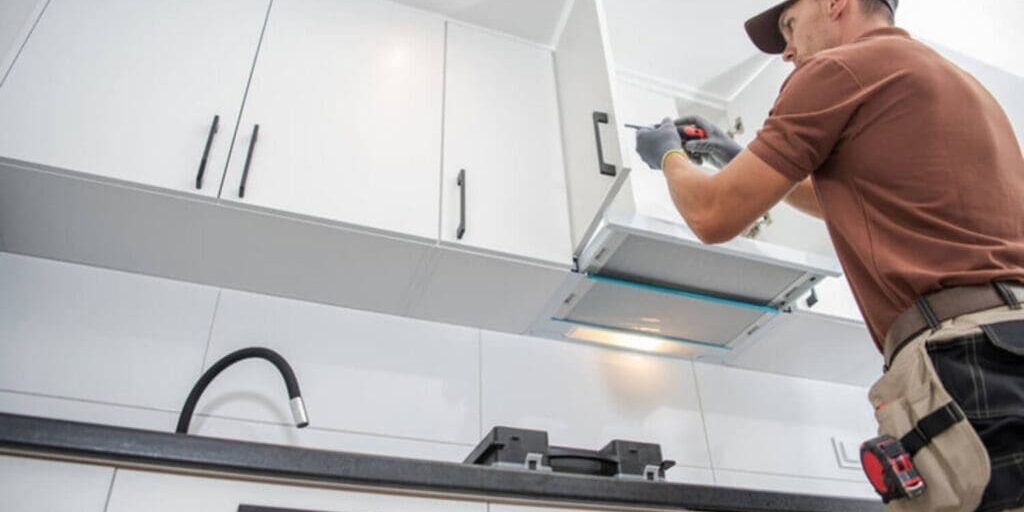 A professional installer working on white kitchen cabinets, illustrating how cabinet refacing works step by step in an Oakland County home.