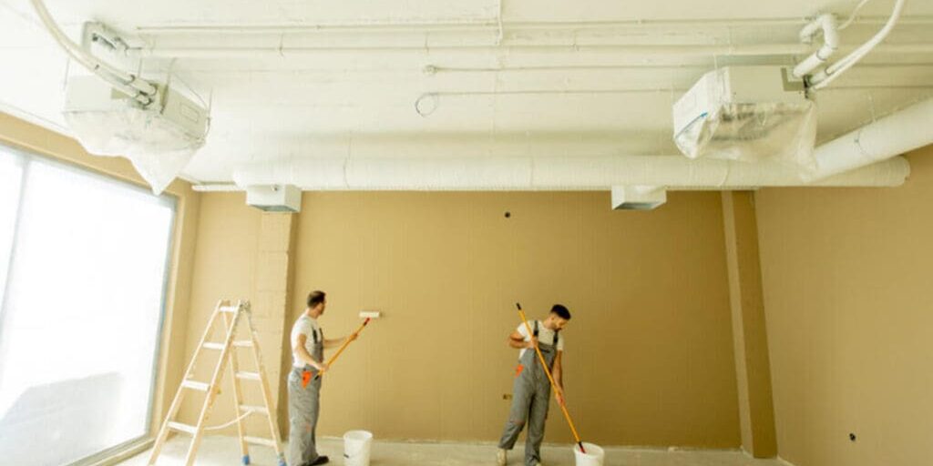 Two professional painters rolling paint on the interior walls of a commercial facility, illustrating how facility maintenance painting works in an active building.